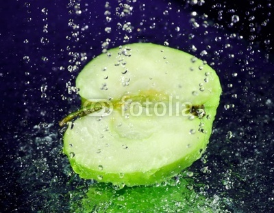 Half of green apple with stopped motion water drops on deep blue